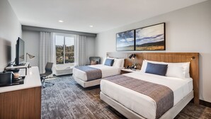 Habitación de hotel con dos camas, un escritorio con computadora, una silla y un ventanal con vistas al paisaje.