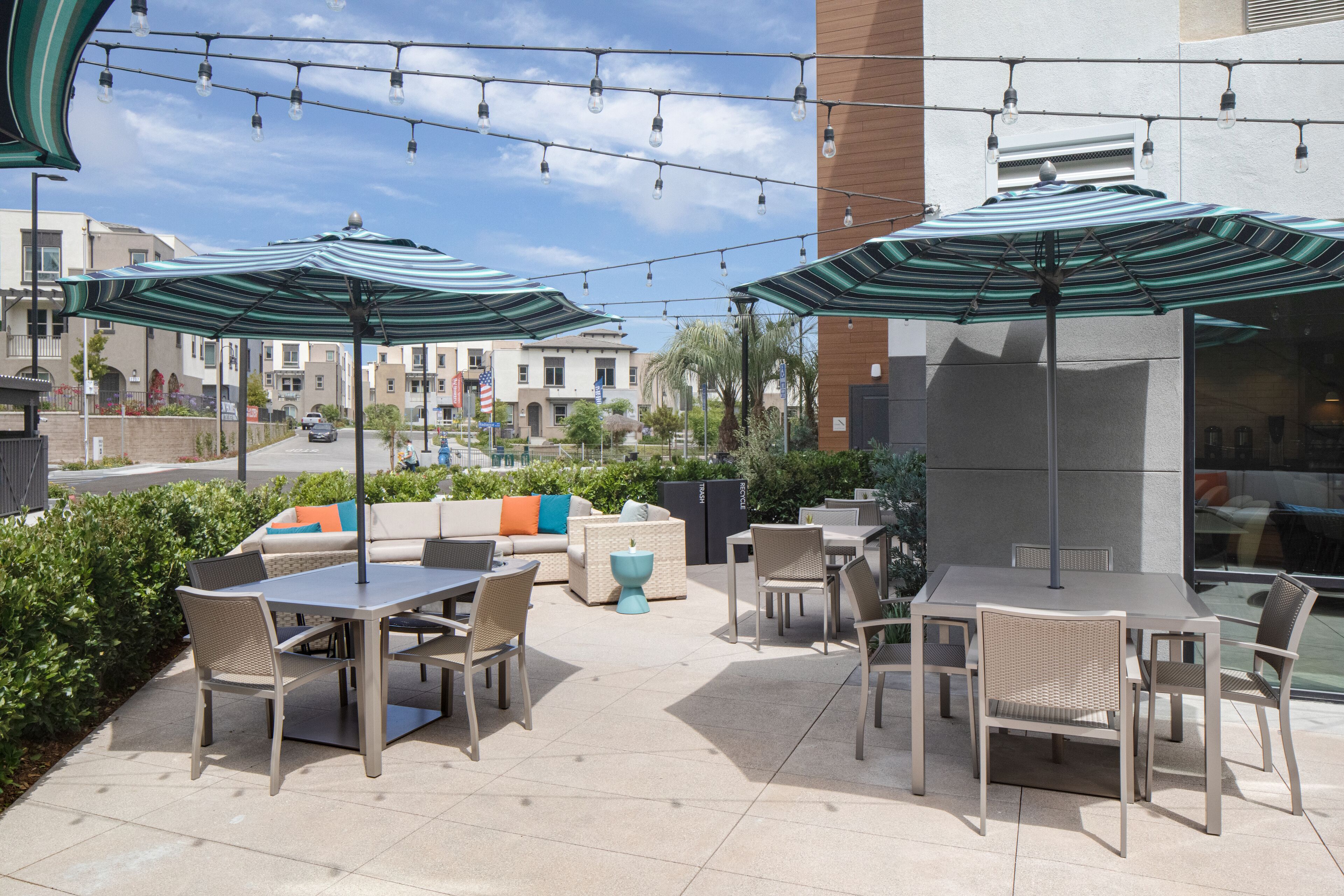 An outdoor patio area with tables and chairs, striped umbrellas, and a sofa with colorful cushions.