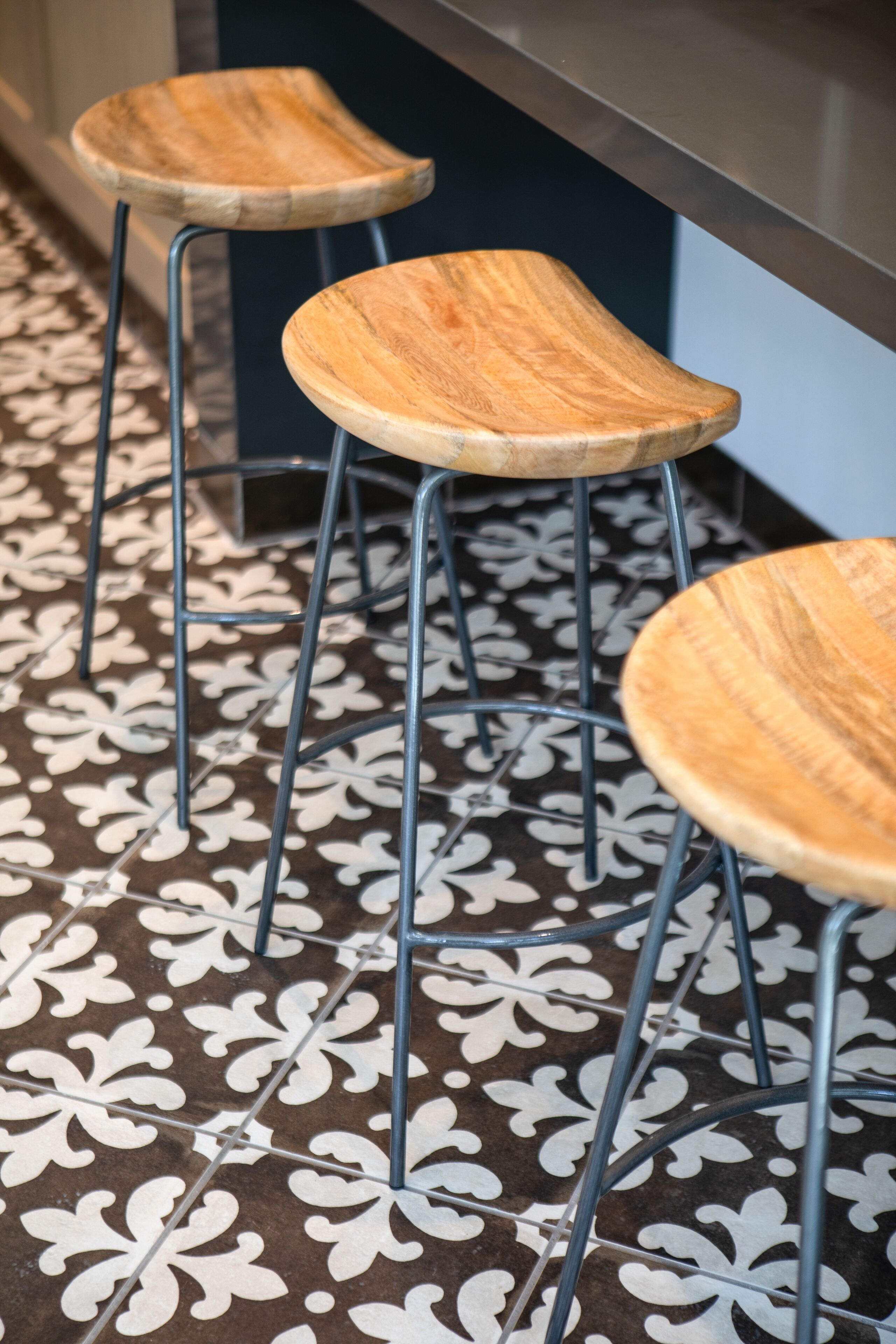Three wooden stools with metal legs on a patterned floor.