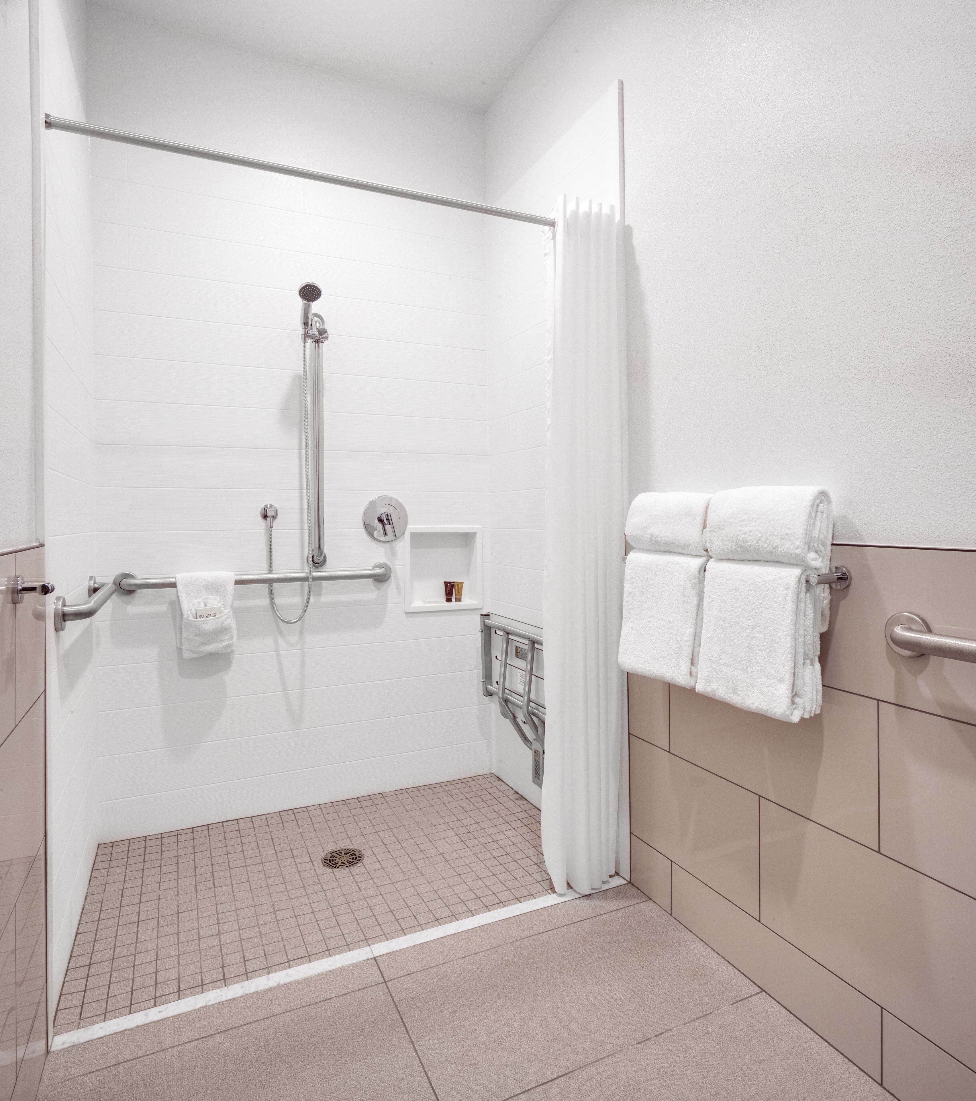 A modern bathroom with a walk-in shower, grab bars, a towel rack, and a hand dryer.
