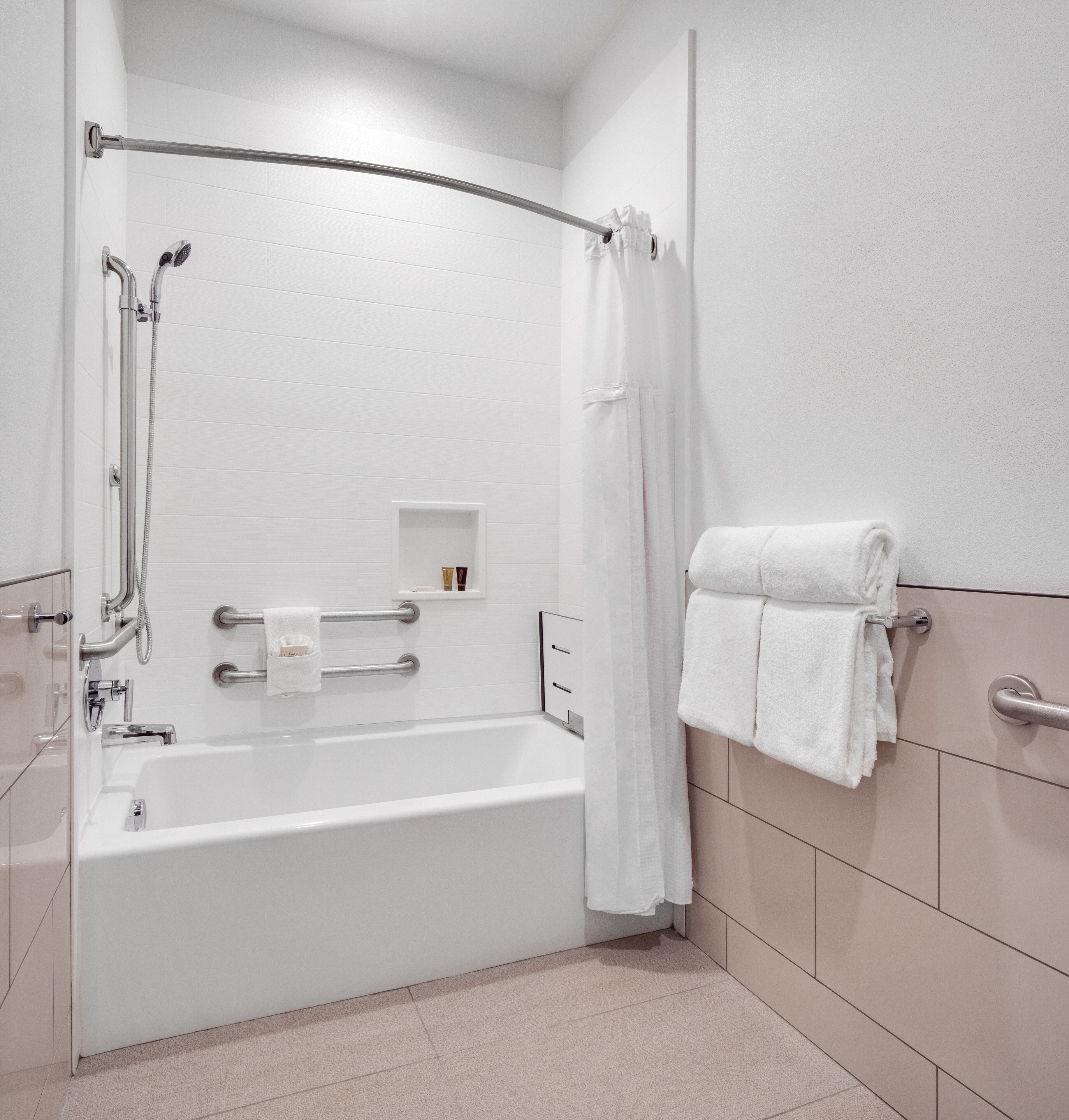 A modern bathroom with a bathtub, shower, and handrails.
