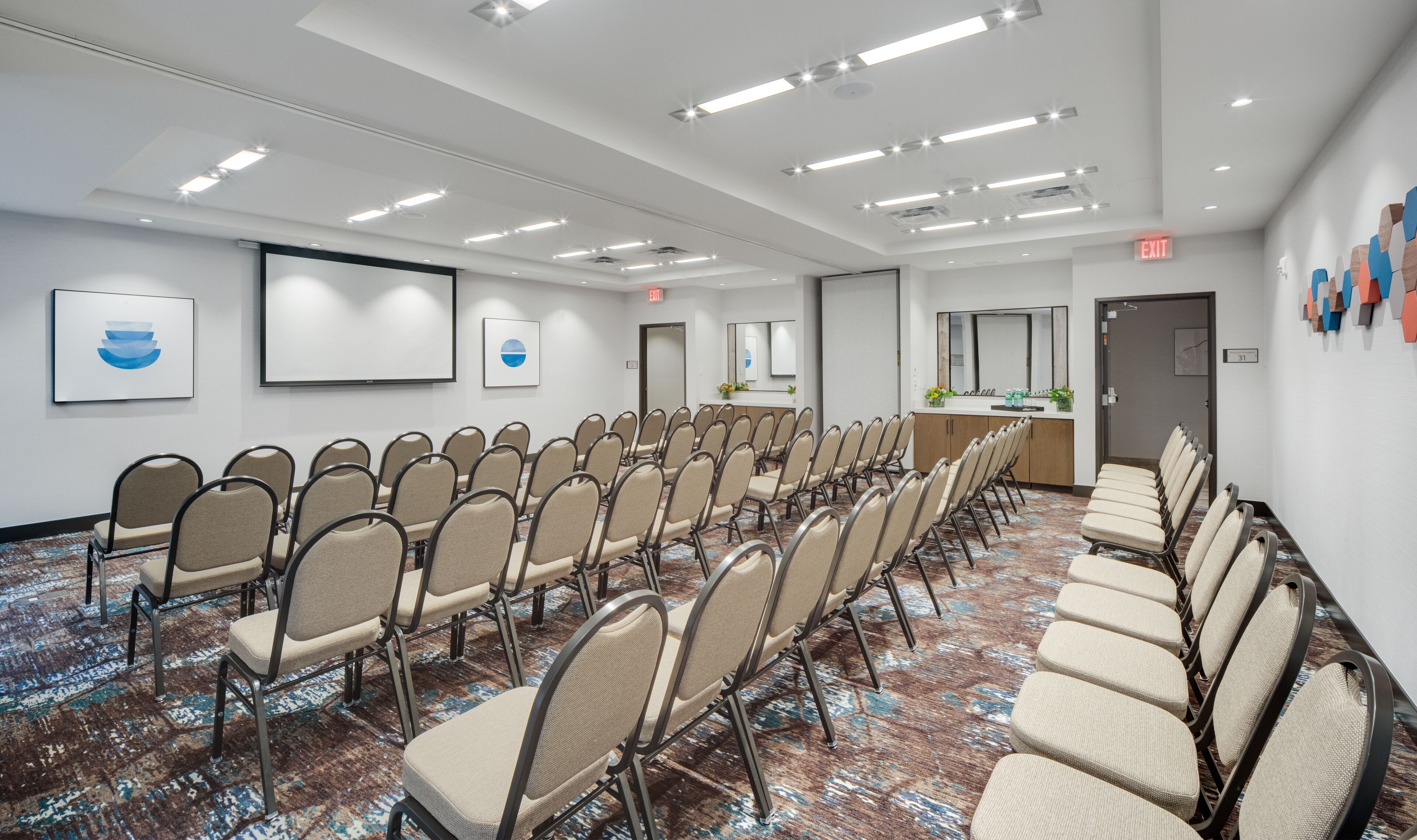 A conference room with rows of chairs, a projector screen, and a reception area with a counter and decorative items.