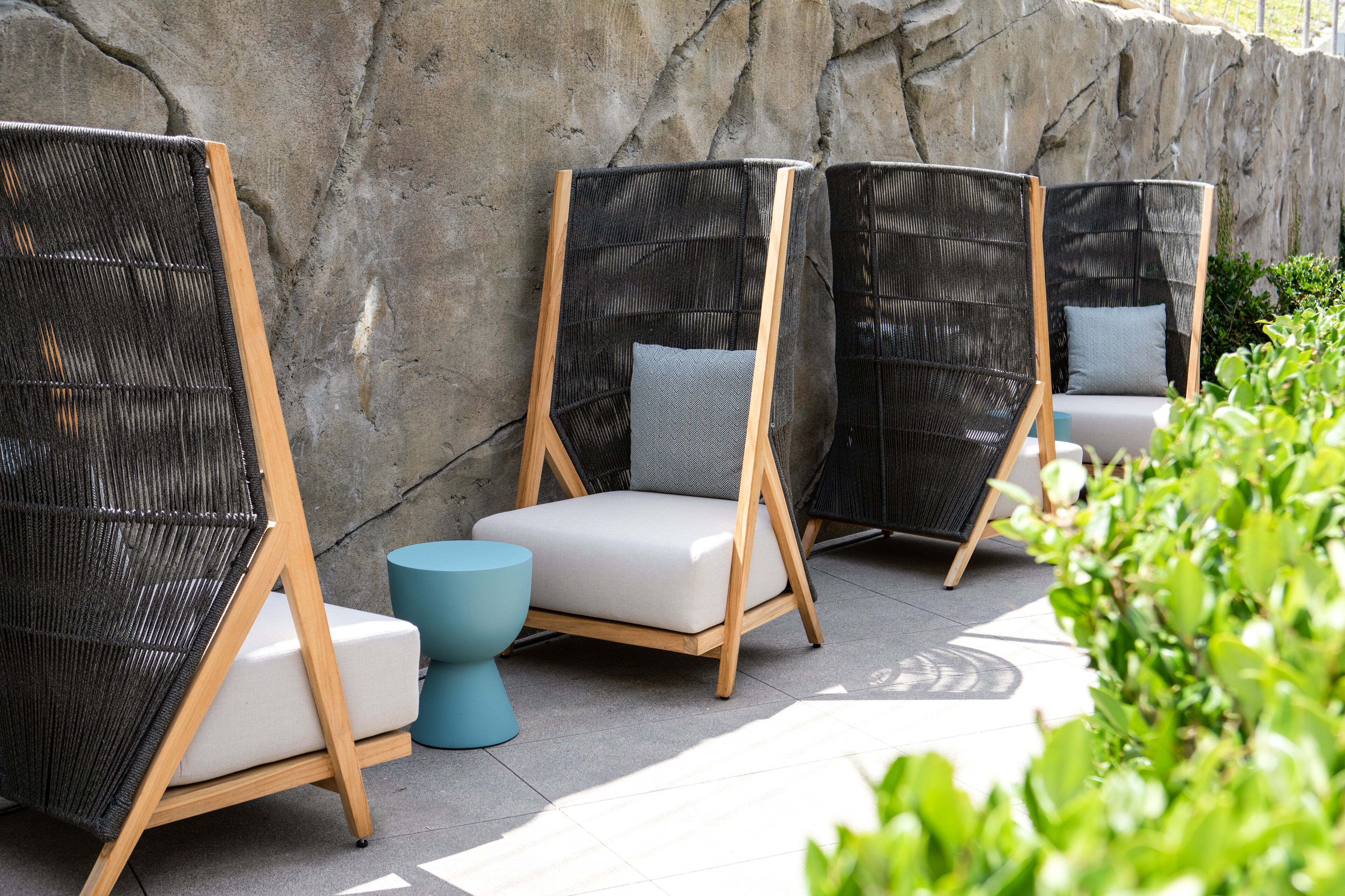 Outdoor seating with wicker chairs and cushions, a stone wall, and a tiled floor.