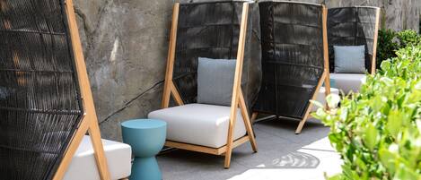 Outdoor seating with wicker chairs and cushions, a stone wall, and a tiled floor.