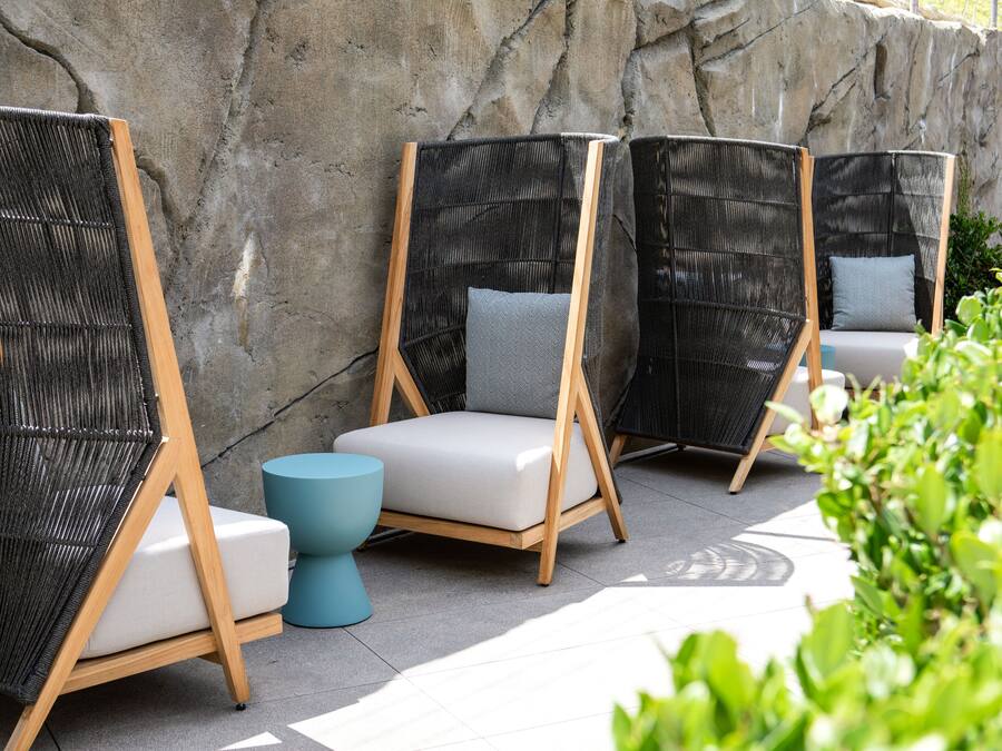 Outdoor seating with wicker chairs and cushions, a stone wall, and a tiled floor.