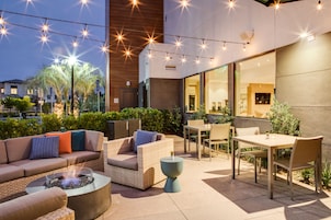 Un patio exterior con un conjunto de sofá, una mesa y sillas. Hay un brasero y luces colgantes.