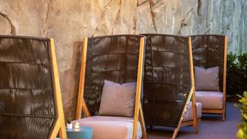 Outdoor seating with wicker chairs and cushions, a stone wall, and string lights.
