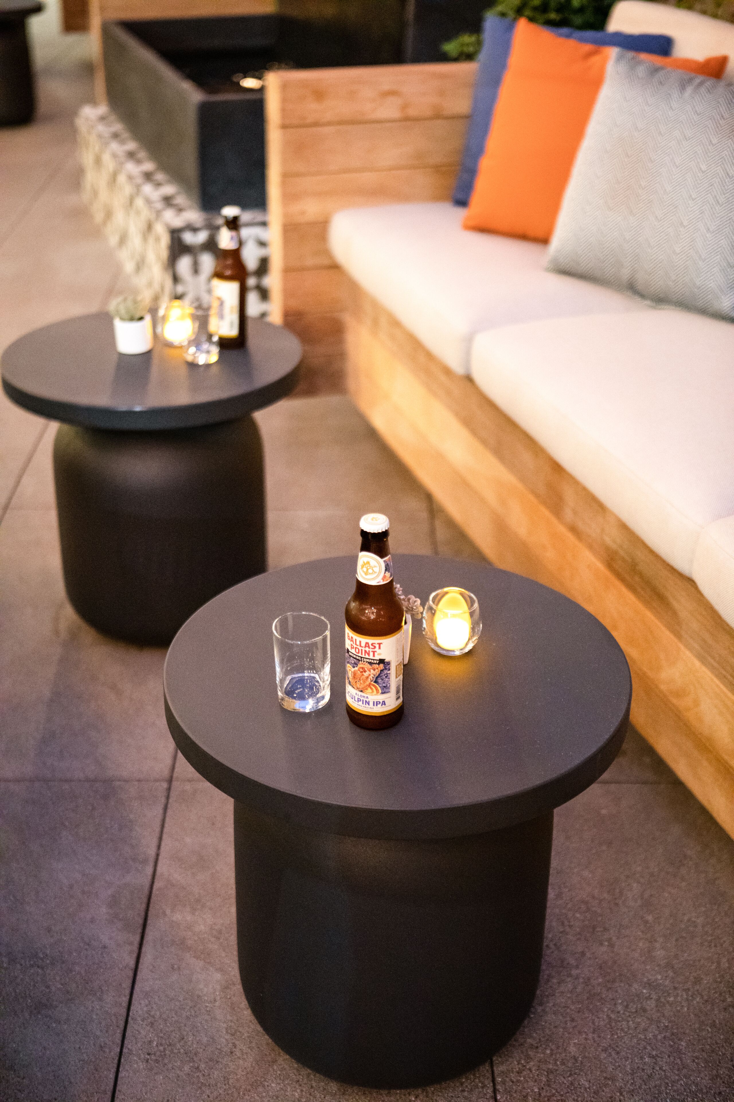 A cozy outdoor seating area with two round tables, each with a bottle of beer and a glass.