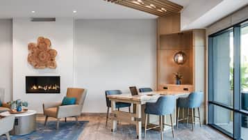 A modern living room with a fireplace, a dining area with a wooden table and chairs, and a large window offering a view of the outdoors.