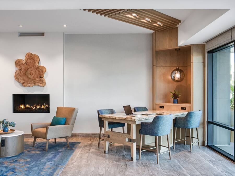 A modern living room with a fireplace, a dining area with a wooden table and chairs, and a large window offering a view of the outdoors.