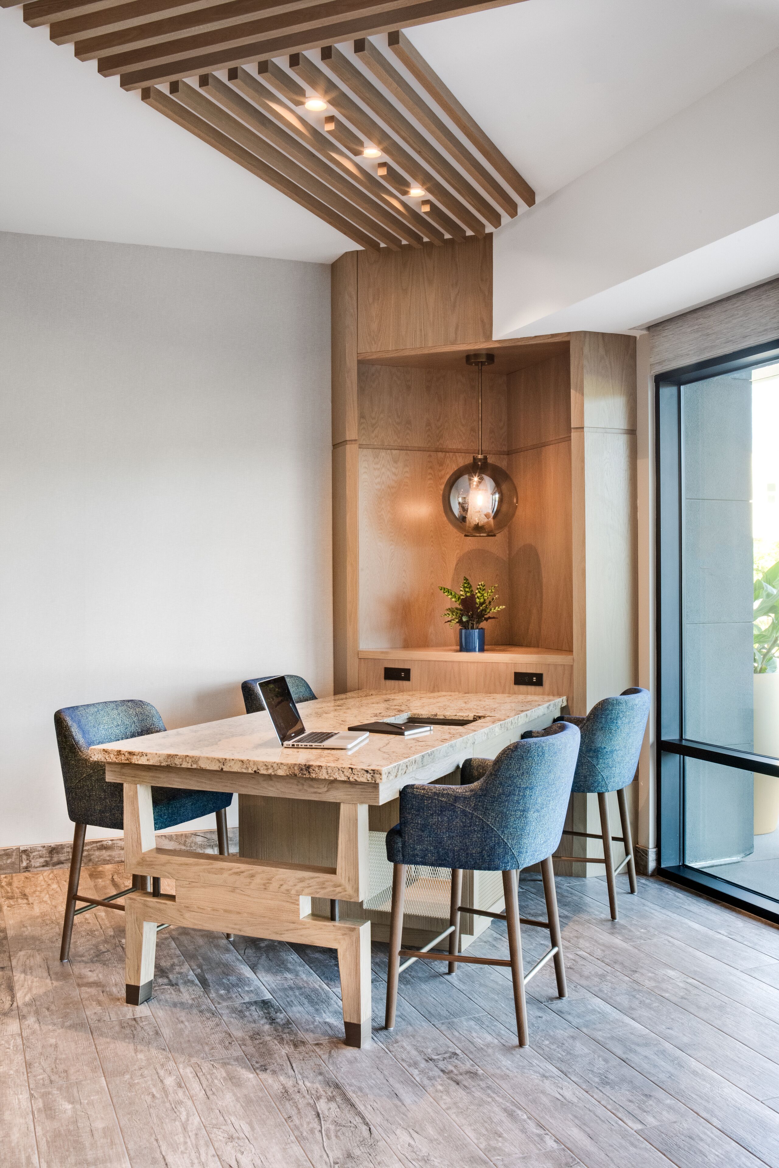 Un comedor moderno con una mesa y sillas de madera, una planta en maceta y una lámpara colgante.