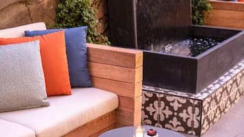 Un área de estar exterior con pared de piedra, un hogar integrado y una mesa redonda con una vela.