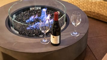 Fuego exterior circular con recinto de vidrio, dos copas de vino y una botella de vino en un patio.