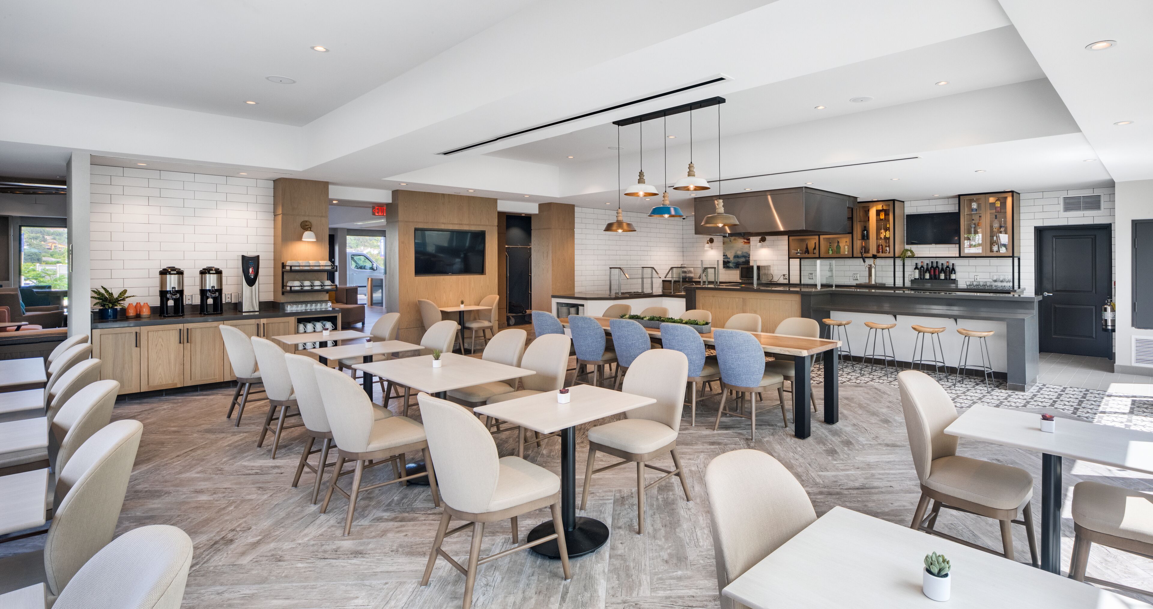 A modern restaurant with multiple dining areas, a bar, and a kitchen visible in the background.