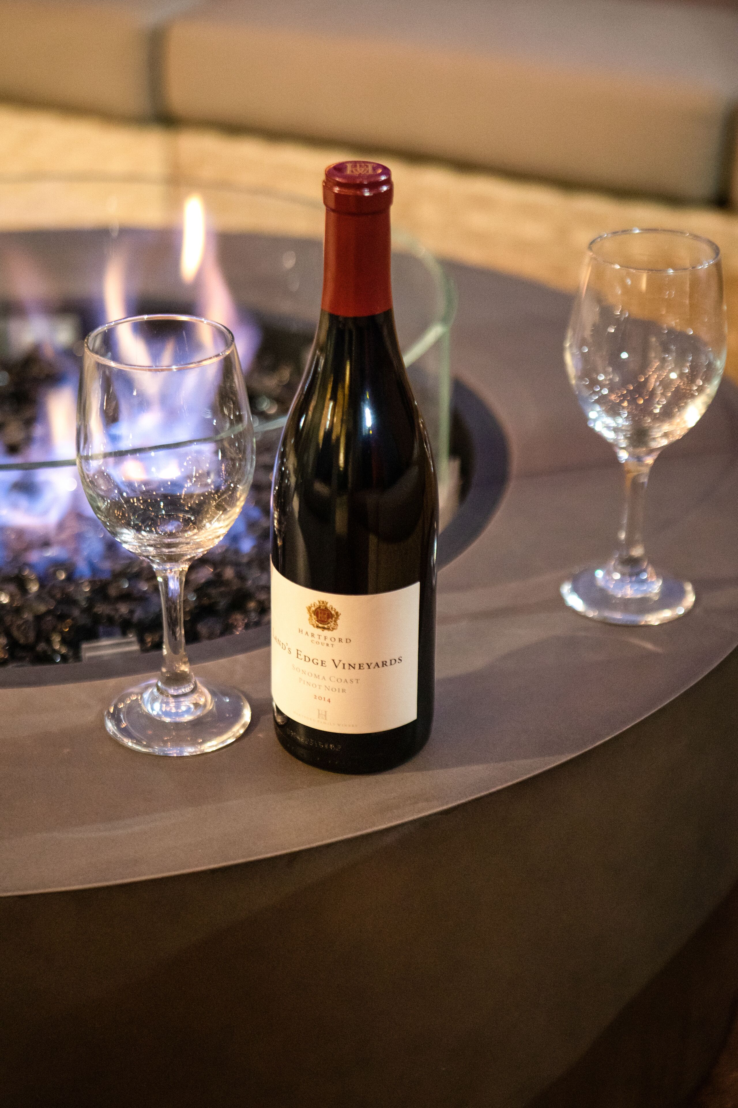 Una botella de vino y dos copas sobre una mesa, con una chimenea al fondo.