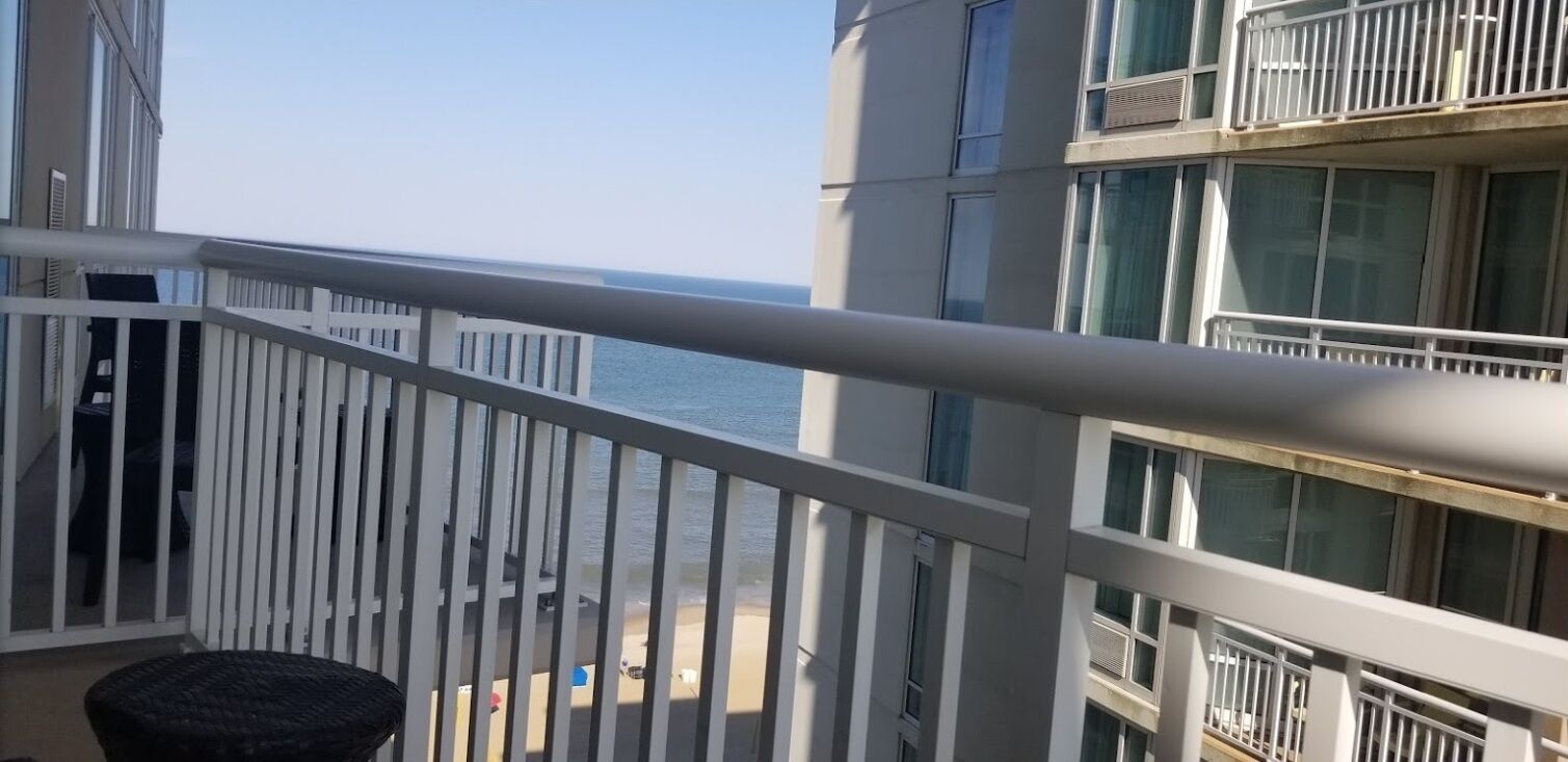 Un balcon avec vue sur la mer, un immeuble doté de nombreuses fenêtres et un fauteuil en osier.
