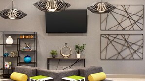 A modern living room with a grey sofa, a flat-screen TV, geometric wall art, and a bookshelf with decorative items.