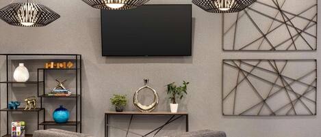 A modern living room with a grey sofa, a flat-screen TV, geometric wall art, and a bookshelf with decorative items.