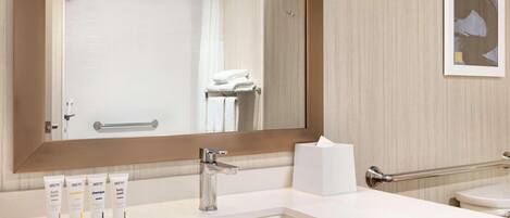 A modern bathroom with a large mirror, white sink, and a vanity area.