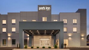 A modern hotel with a 'Park Inn by Radisson' sign, featuring a covered entrance, multiple windows, and a parking lot.