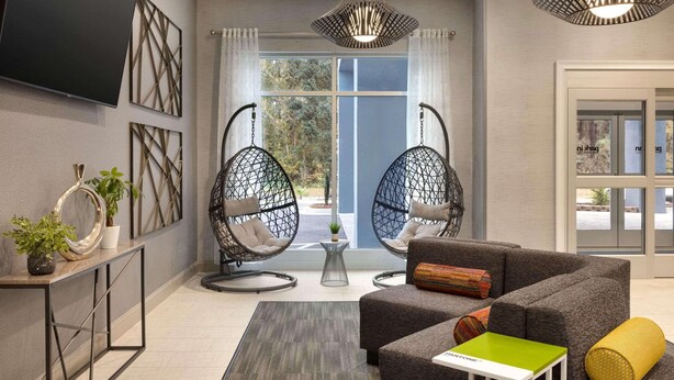 A modern living room with a grey sofa, two black hanging chairs, a small table, and a TV mounted on the wall.