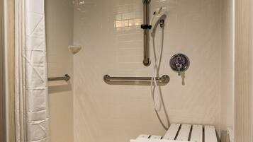 Ducha a pie con paredes de azulejos blancos, cabezal de ducha manual, accesorio de ducha manual, barra de apoyo y toallero.