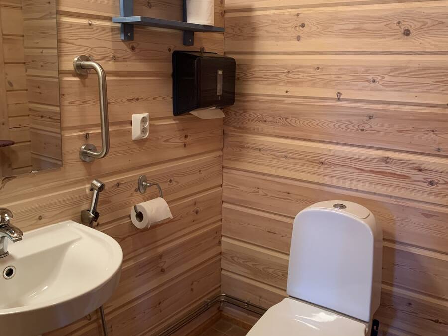 Un baño con pared de madera, un lavamanos blanco, un inodoro, un espejo y una estantería con una toalla.