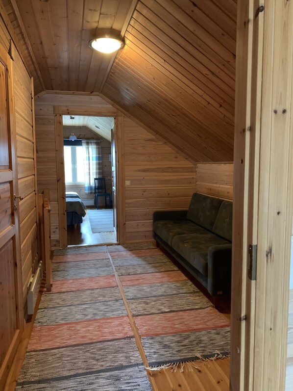 Un interior de madera con techo inclinado, un sofá y un tapete estampado.