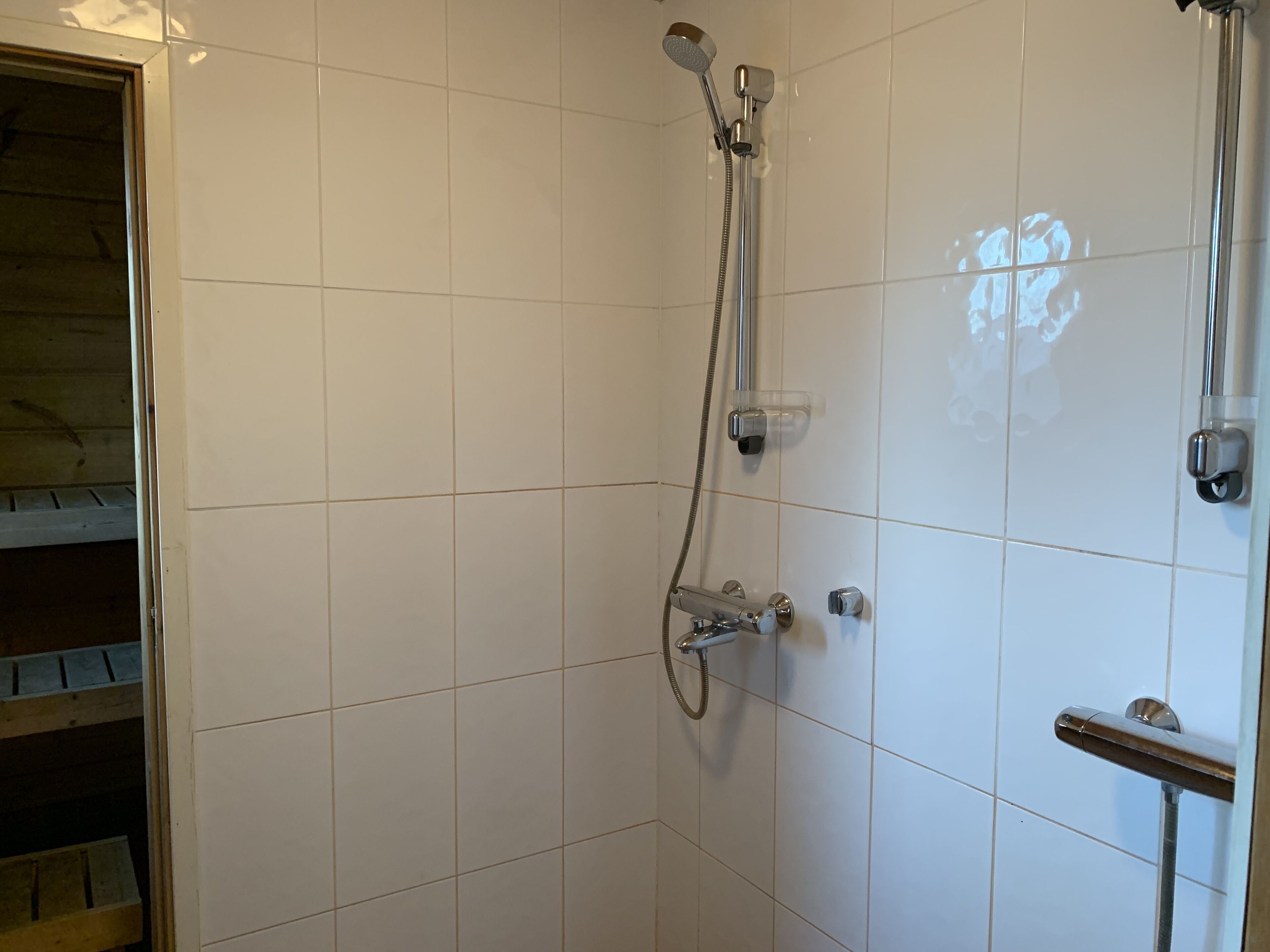 A shower with a handheld showerhead and a wall-mounted faucet.