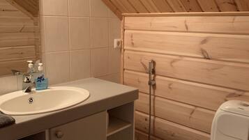 Un baño pequeño y funcional con techo de madera, un lavamanos blanco con espejo, inodoro y ducha.