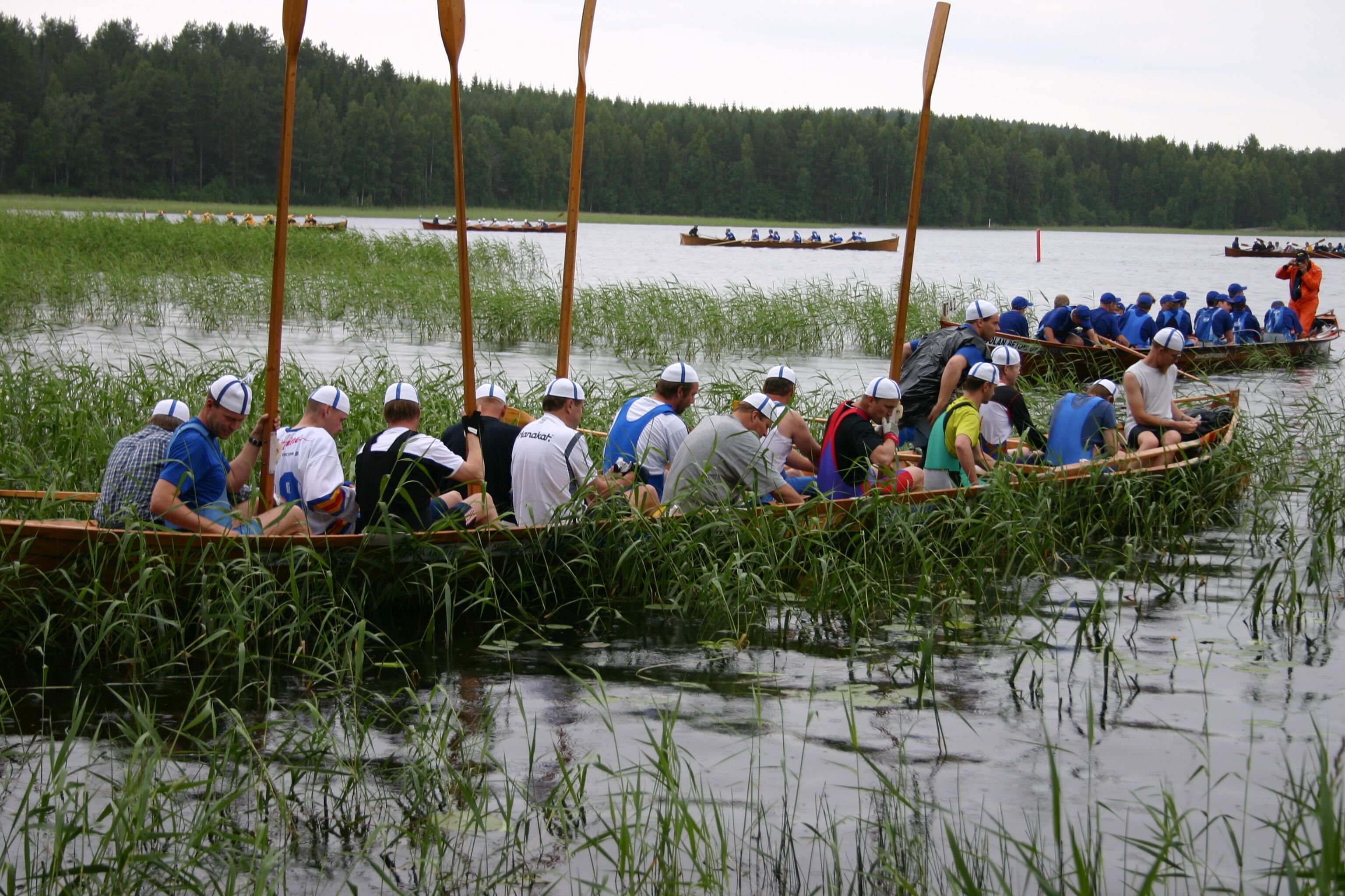Eine Gruppe von Menschen in einem Boot auf einem Fluss, umgeben von hohem Gras und Bäumen.