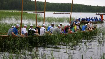 Eine Gruppe von Menschen in einem Boot auf einem Fluss, umgeben von hohem Gras und Bäumen.