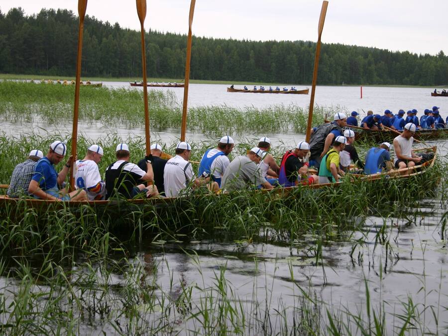 Eine Gruppe von Menschen in einem Boot auf einem Fluss, umgeben von hohem Gras und Bäumen.