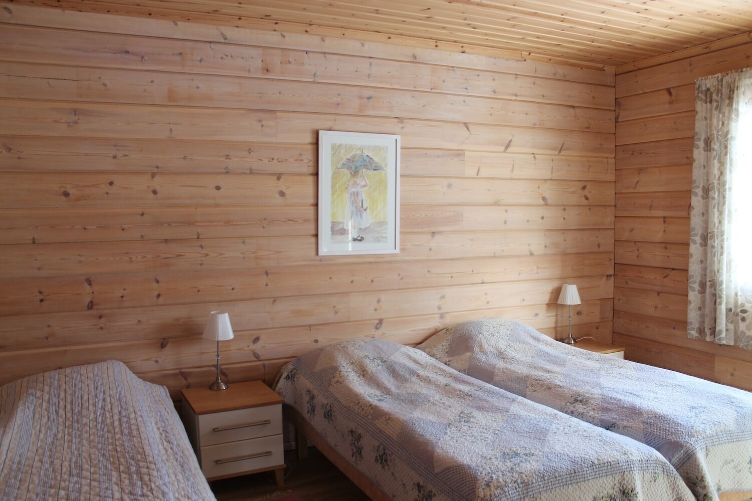 A wooden-paneled room with two beds, a nightstand with a lamp, and a framed picture on the wall.