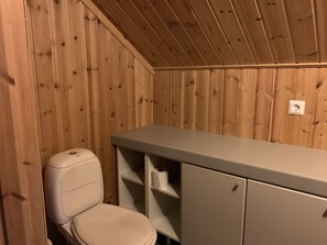 A small, compact bathroom with wooden walls and a single toilet. - Lomakivi (Iitti)