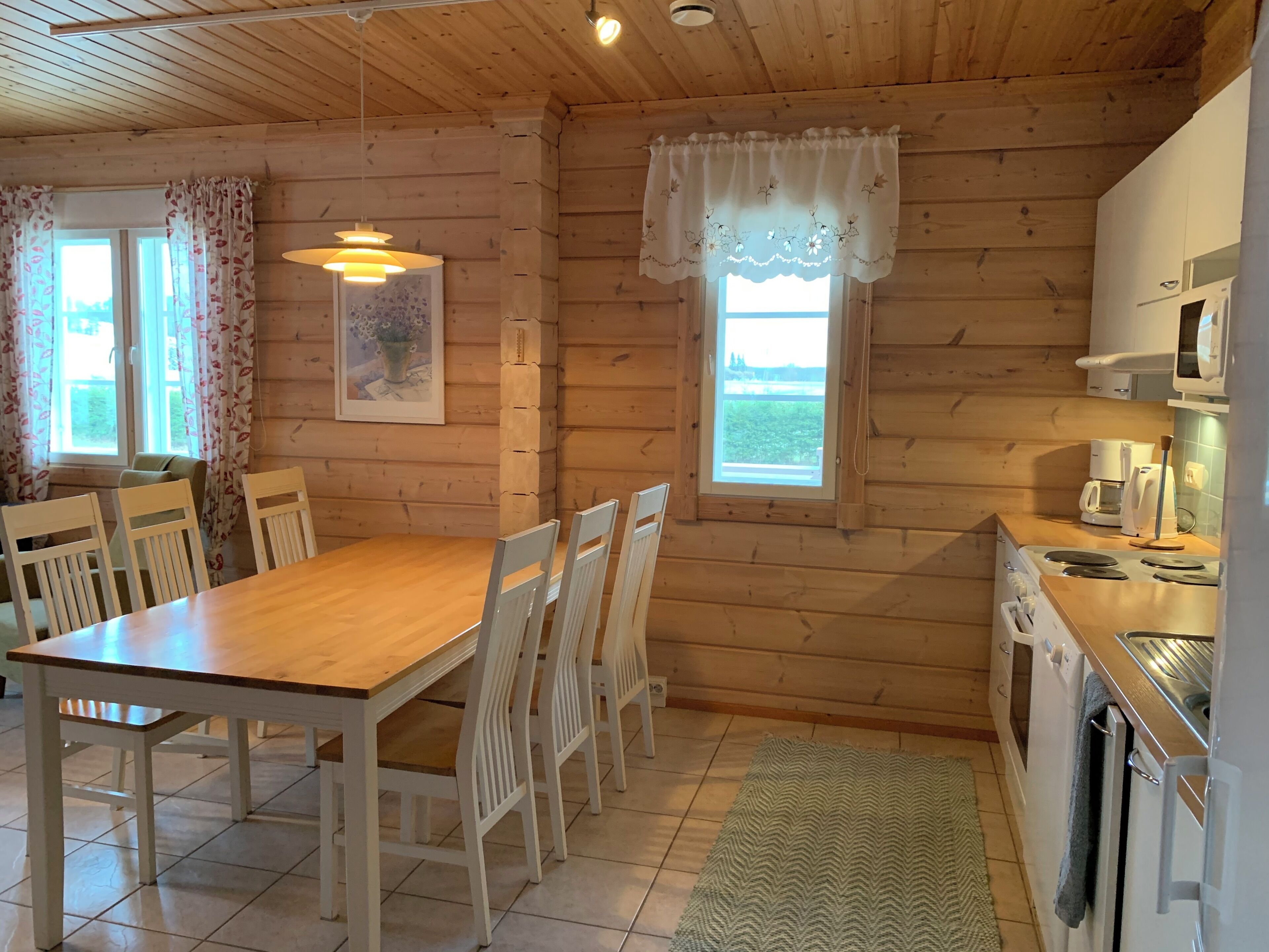 Un interno in legno con tavolo da pranzo, sedie, angolo cottura e finestra con tende.
