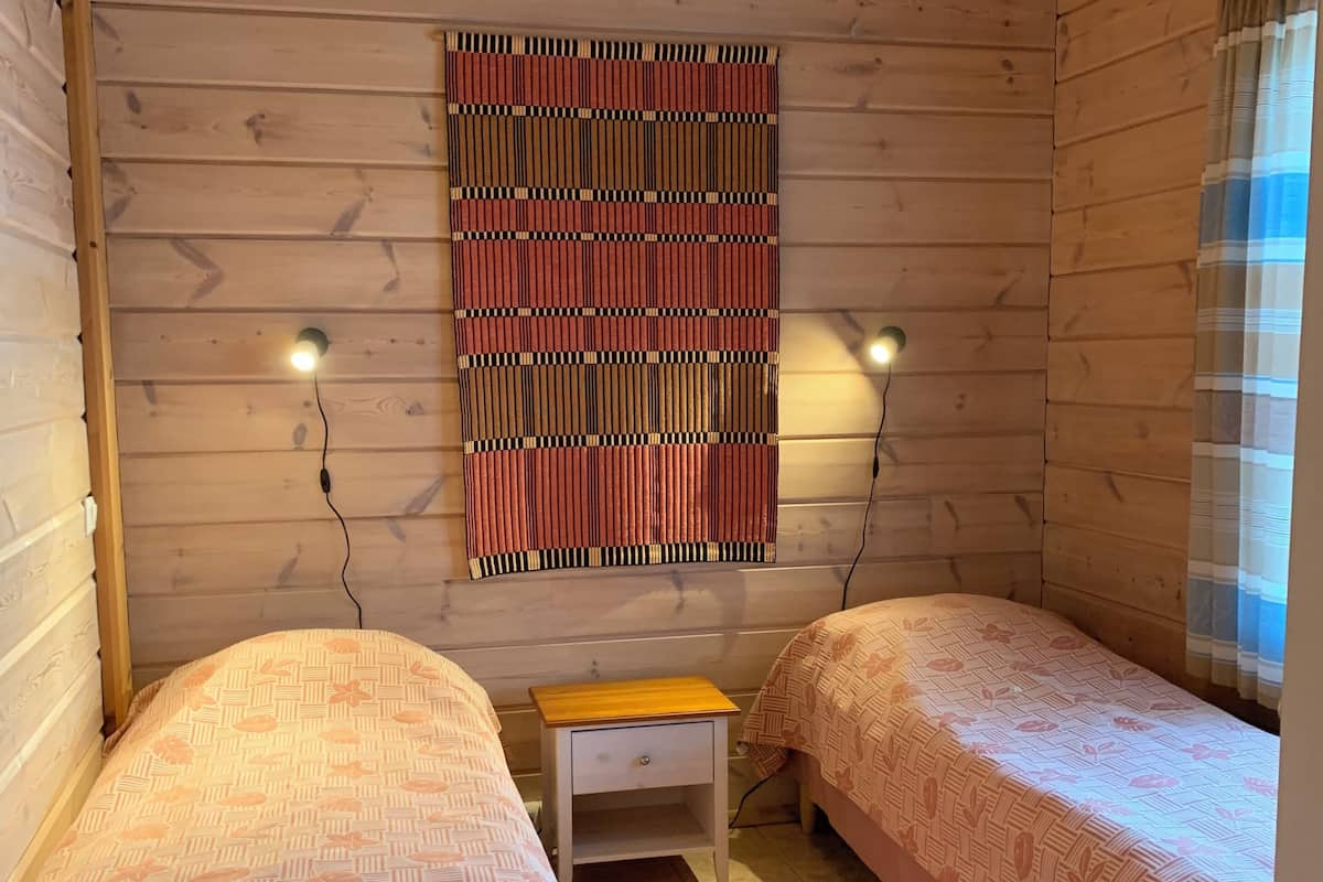 A room with two beds, a small wooden nightstand, a patterned wall hanging, and two wall-mounted lights.