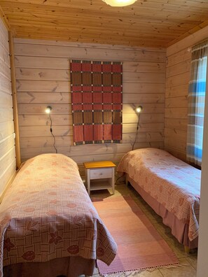 A room with two beds, a small wooden nightstand, a patterned wall hanging, and two wall-mounted lights. - Lomakivi (Iitti)