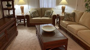 A living room with two sofas, a coffee table, and a wooden cabinet. There are two lamps on side tables and a window with curtains. - Swan Lake House in Sun City Center with 60' Screened Lanai (Sun City Center)