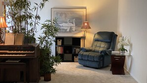 A living room with a piano, a large chair, a bookshelf, and a framed picture on the wall. - Swan Lake House in Sun City Center with 60' Screened Lanai (Sun City Center)