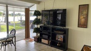 A living room with a TV, shelves, a plant, and a dining area with a table and chairs. - Swan Lake House in Sun City Center with 60' Screened Lanai (Sun City Center)