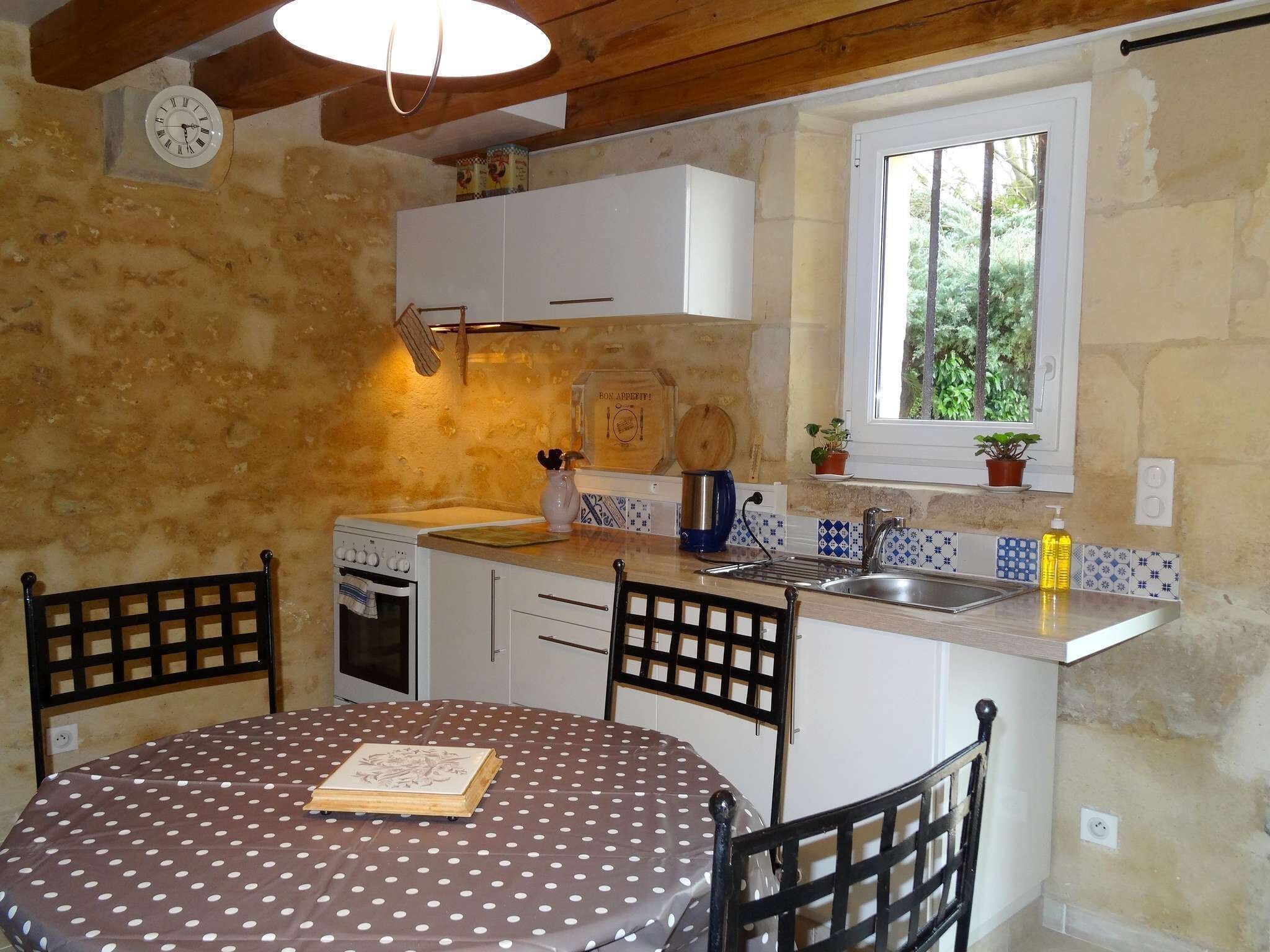 A compact kitchen with a dining table, chairs, a clock, and a window with a view of greenery.