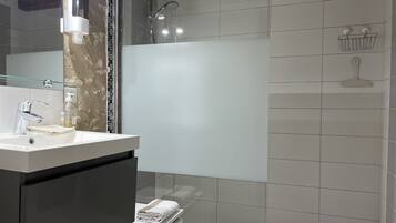 A modern bathroom with a glass shower enclosure, a white sink with a soap dispenser, and a towel rack.