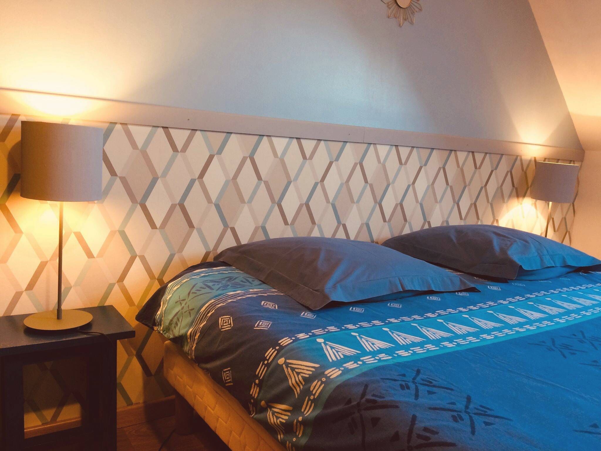 Un dormitorio con un cabecero de diseño geométrico, una cama con ropa de cama estampada y dos lámparas de noche.
