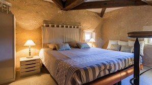 A rustic bedroom with exposed wooden beams, a large bed with striped bedding, and bedside lamps. - Gites de Gondières (Saint-Eloi)