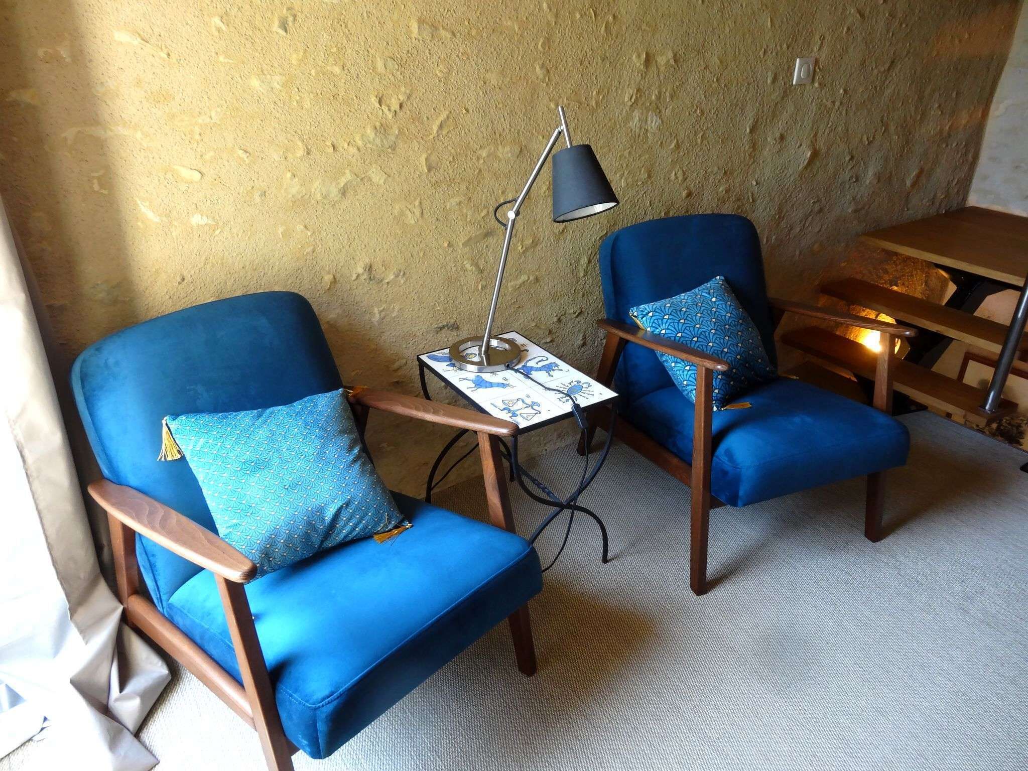 A room with two blue armchairs, a small table with a lamp, and a wooden table.