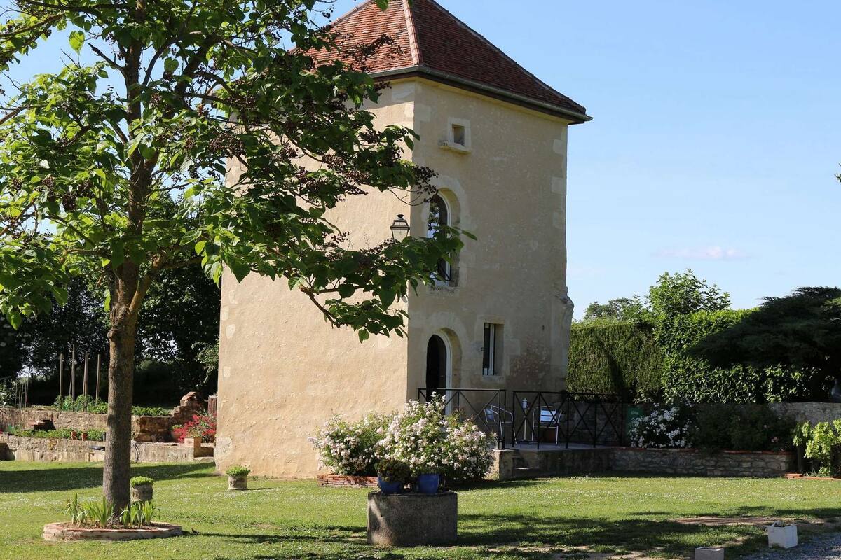 Un bâtiment historique doté d’une tour, entouré d’un jardin bien entretenu, agrémenté de plantes en pot et d’une pelouse.