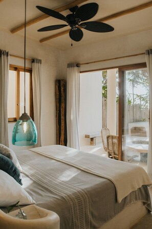 Un dormitorio con cama, ventilador de techo, lámpara colgante y vista al exterior.
