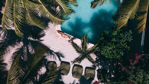 An aerial view of a tropical resort with a clear blue pool surrounded by palm trees and a sandy beach. - Zorba Tulum Beach Homes (Tulum)