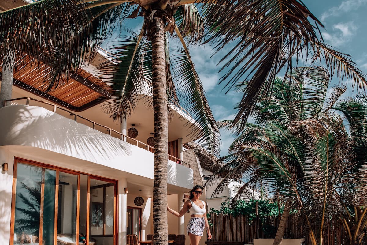 A poolside area with a palm tree, a pool, and a building with large windows and a balcony.